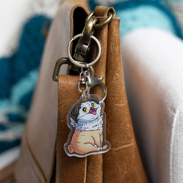Acrylic keychain of Potroast, body and face of a pug with the beak and feathers of an owl clipped to a leather purse. From Bookshops and Bonedust.