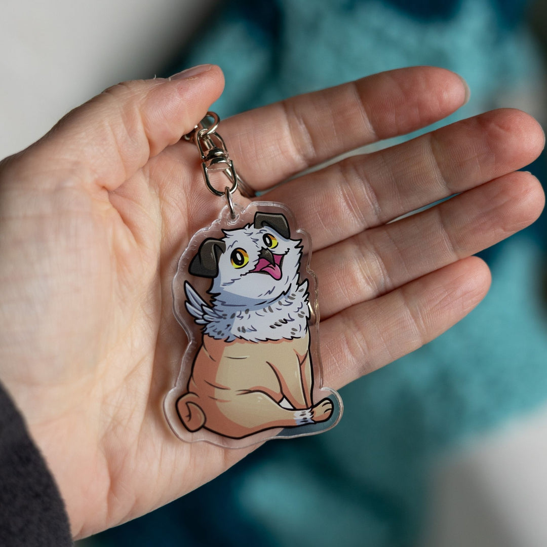  Acrylic keychain of Potroast, body and face of a pug with the beak and feathers of an owl held in a palm. From Bookshops and Bonedust.
