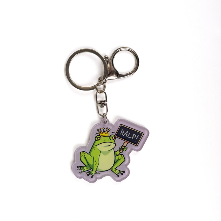 Acrylic keychain of a green frog wearing a crown holding up a chalk board sign that reads ‘HALP!’

