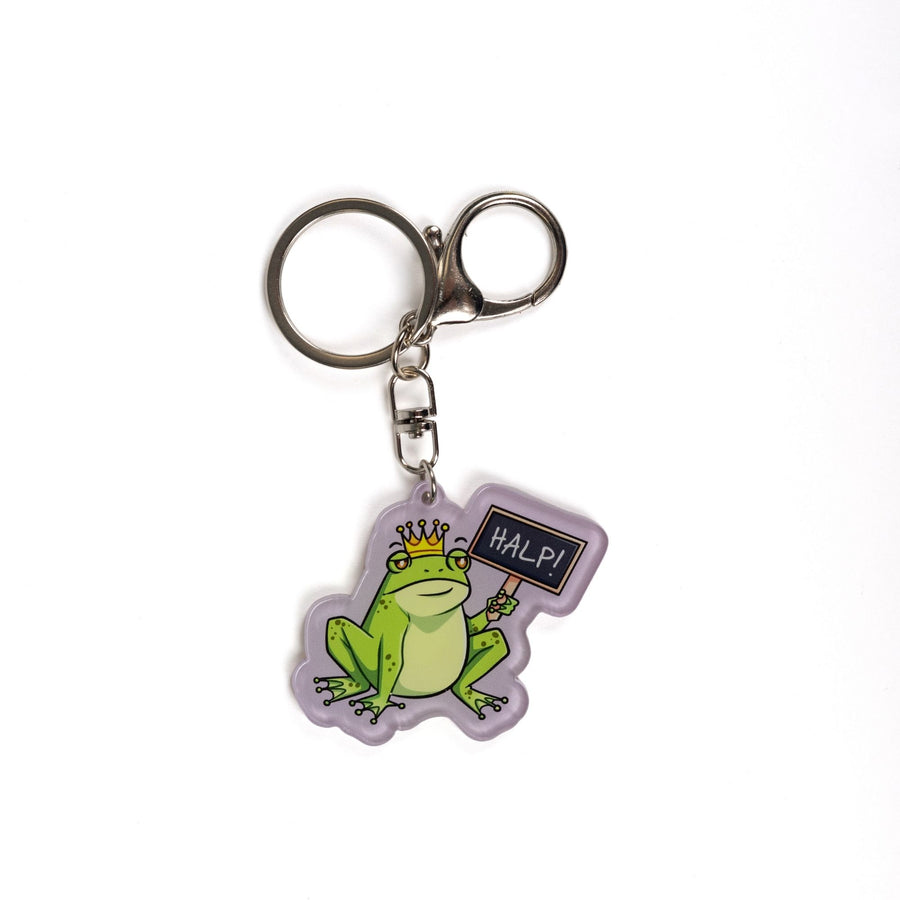 Acrylic keychain of a green frog wearing a crown holding up a chalk board sign that reads ‘HALP!’

