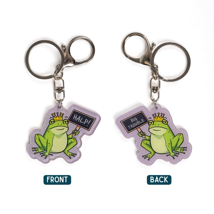 2 acrylic keychains of a green frog wearing a crown holding up a chalk board sign. One side reads ‘HALP!’ and the other ‘Big trouble.’ 
