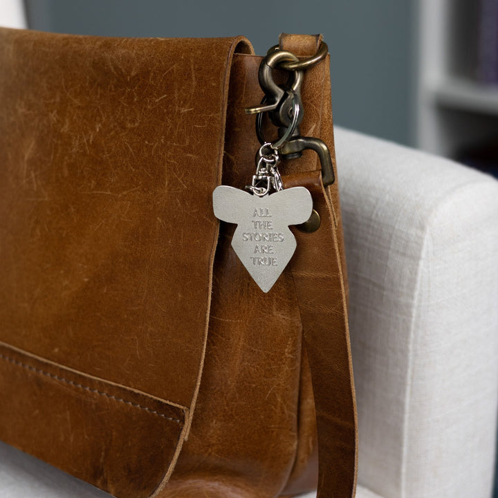 Silver keychain reads ‘All the stories are true,’ clipped to a brown leather purse.