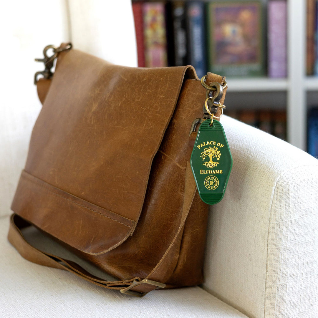  Green motel-style keychain with gold lettering that reads ‘Place of Elfhame’ and a golden tree clipped to a brown messenger bag.