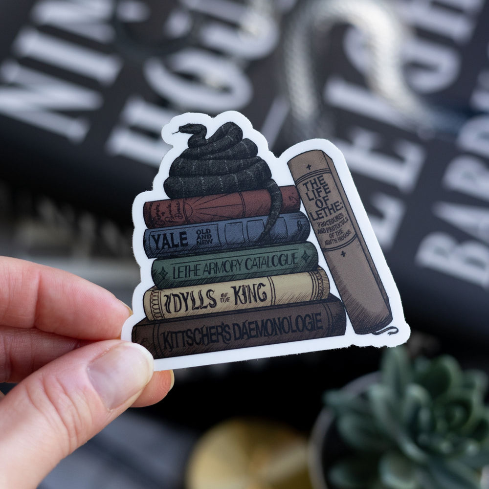 Sticker of stack of books from the Lethe House library with snake on top, held over Ninth House by Leigh Bardugo