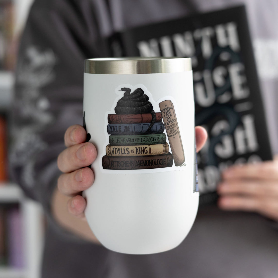Sticker of stack of books from the Lethe House library from Ninth House by Leigh Bardugo with snake on top, on a white tumbler.