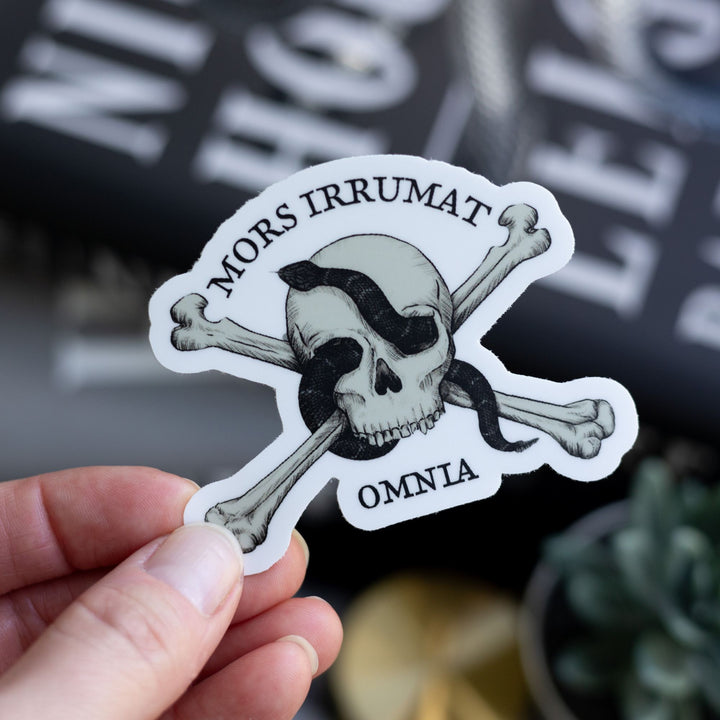  Sticker of skull with snake that reads ‘mors vincit omnia’ held over Ninth House by Leigh Bardugo