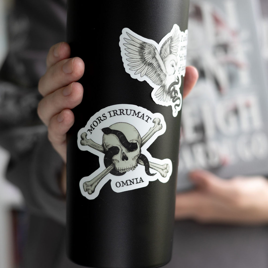  Sticker of skull with snake that reads ‘mors vincit omnia’ on a black tumbler.