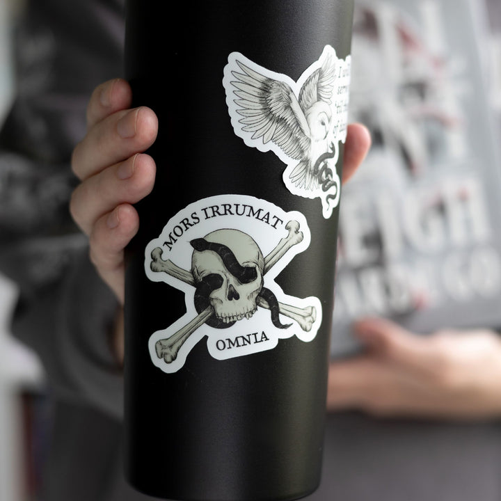  Sticker of skull with snake that reads ‘mors vincit omnia’ on a black tumbler.
