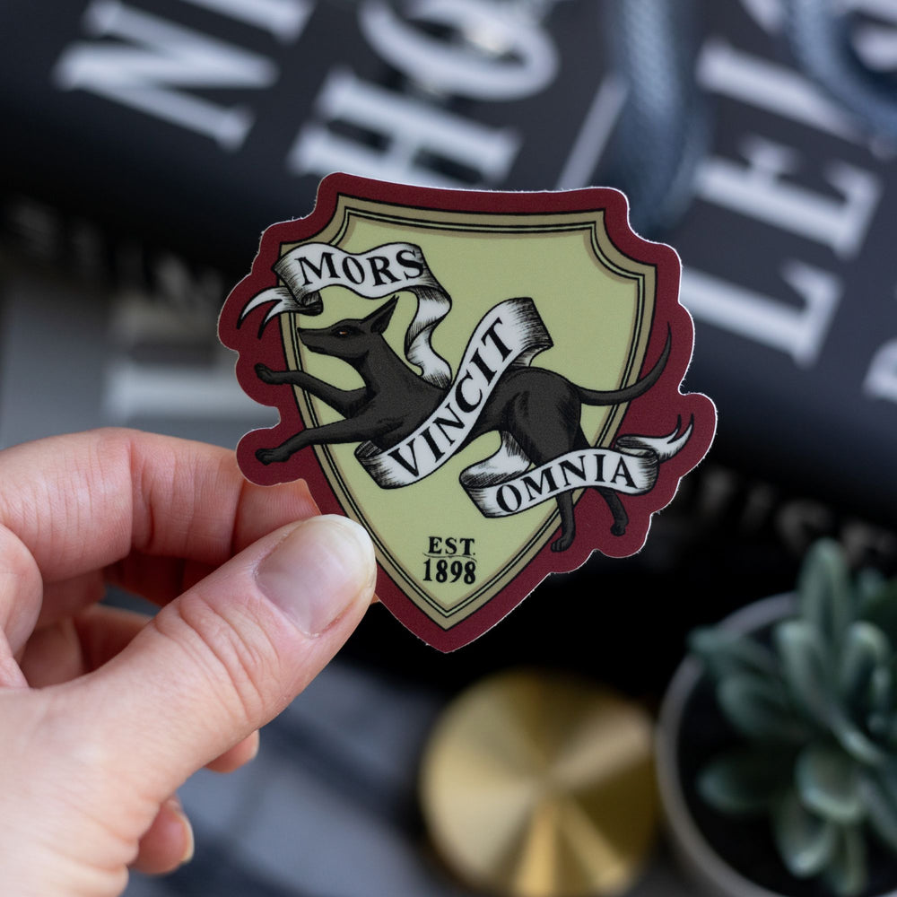 Sticker of the Lethe House jackal, reads ‘Mors Vincit Omnia’ and ‘est. 1898’ held over Ninth House by Leigh Bardugo