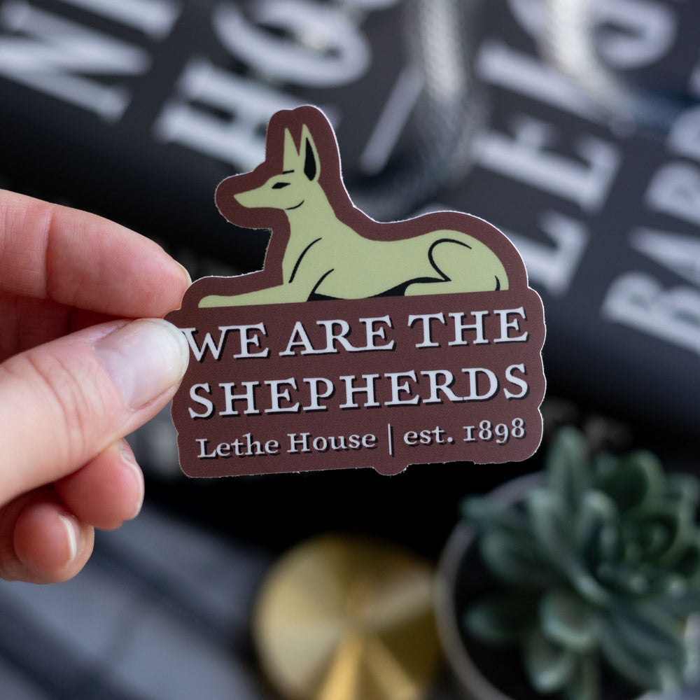 Sticker of Lethe jackal over the words ‘We are the Shepards, Lethe House, est 1898,’ from Ninth House. Held above Ninth House
