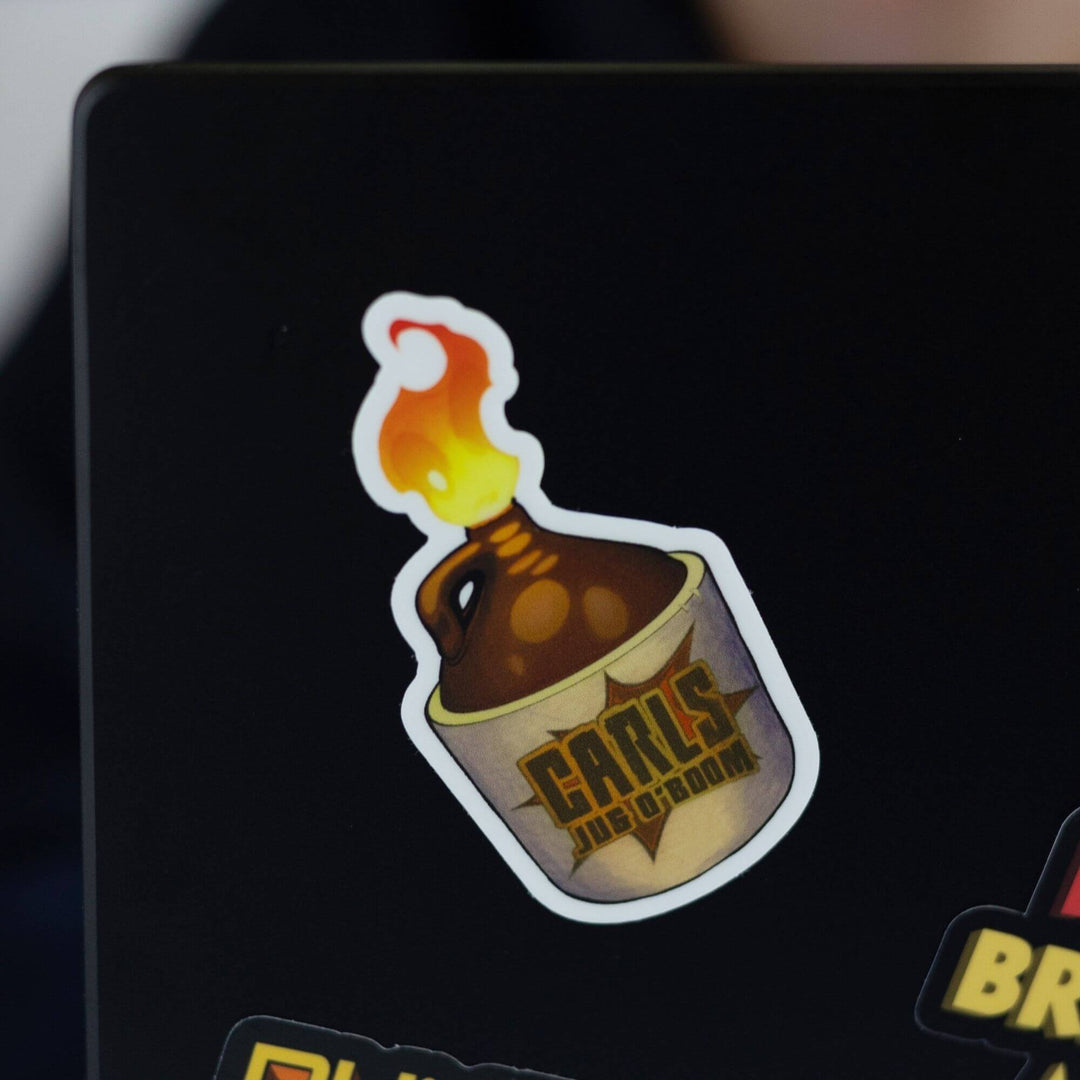 Sticker of an amber glass bottle with a product label that reads ‘Carl's Jug O Boom’ with flames coming out the top. Displayed on the corner of a black laptop.