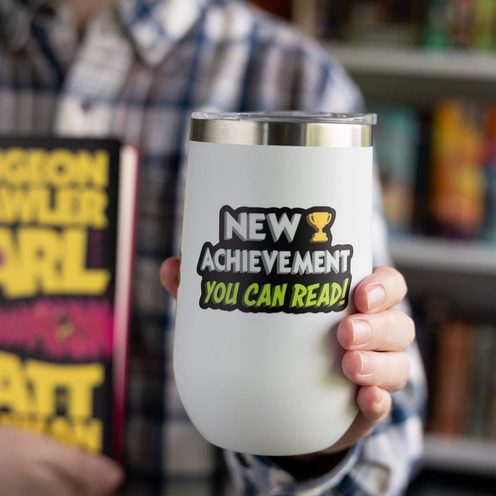 Sticker reads ‘New Achievement You Can Read!’ next to a trophy. Letters are white and green, outlined in black. On a white tumbler.