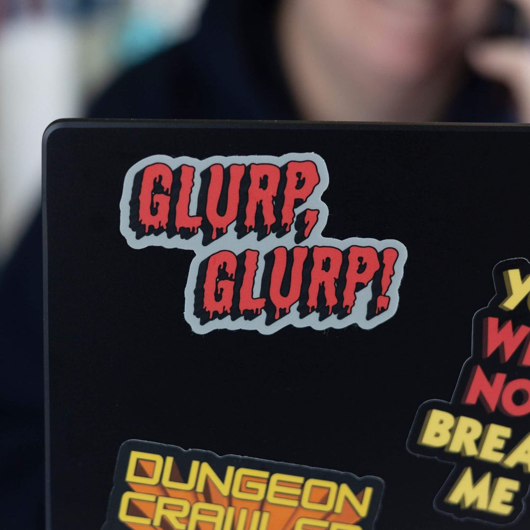 Sticker of the words ‘Glurp,Glurp!’ in red. The words are dripping and on a grey background. From Dungeon Crawler Carl. Displayed on a black laptop