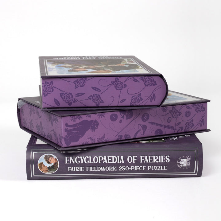 Stack of 3 puzzle boxes showing all sides. Purple edges with pattern of buttons and mushrooms. Spine of the box reads Encyclopaedia of Faeries Faerie Fieldwork 250-piece puzzle.