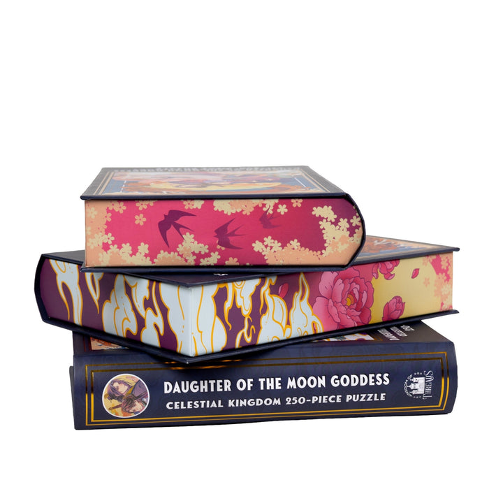 Stack of 3 puzzle boxes showing all sides. Pink and yellow sides with clouds and roses and the spine of the box reads Daughter of the Moon Goddess Celestial Kingdom 250-piece puzzle.