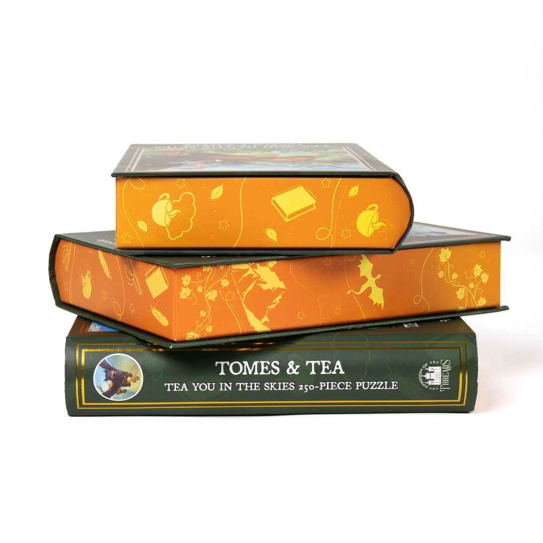 Stack of 3 puzzle boxes showing all sides. Orange edges with yellow teapots and books and the spine of the box reads Tomes and Tea Tea You in the Skies 250-piece puzzle.