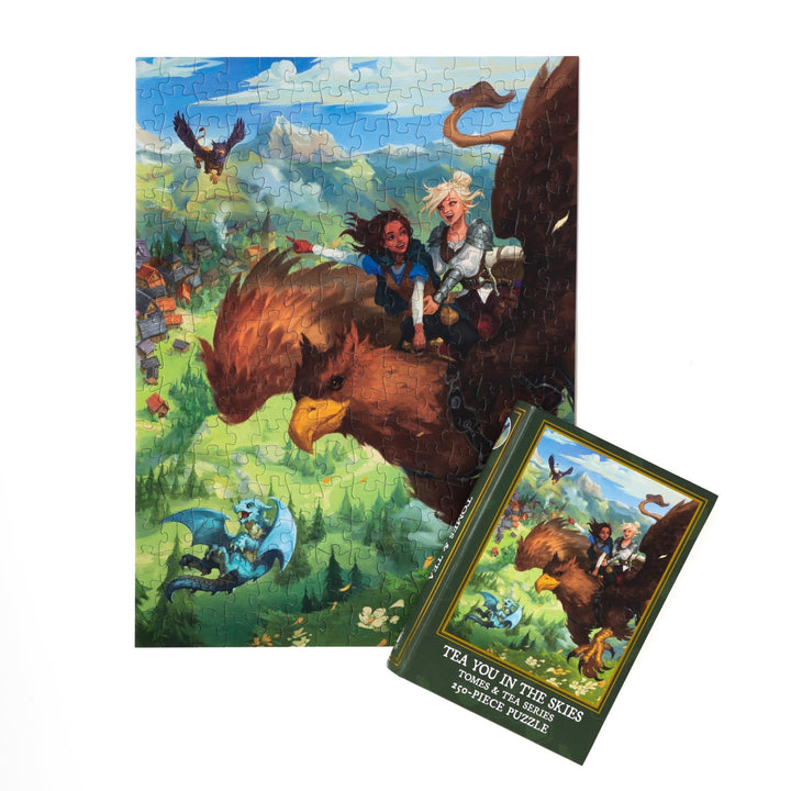 Completed puzzle of Kianthe and Reyna and green, book-shaped box with matching art for Tea You in the Skies Tomes and Tea Series 250-piece puzzle.