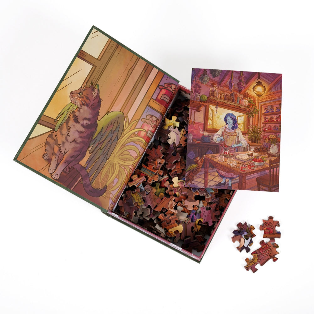 An open book-shaped box reveals puzzle pieces. Inner art on the top flap a tabby cat with green wings. An art print of Kiela making jam in her kitchen atop the pieces.