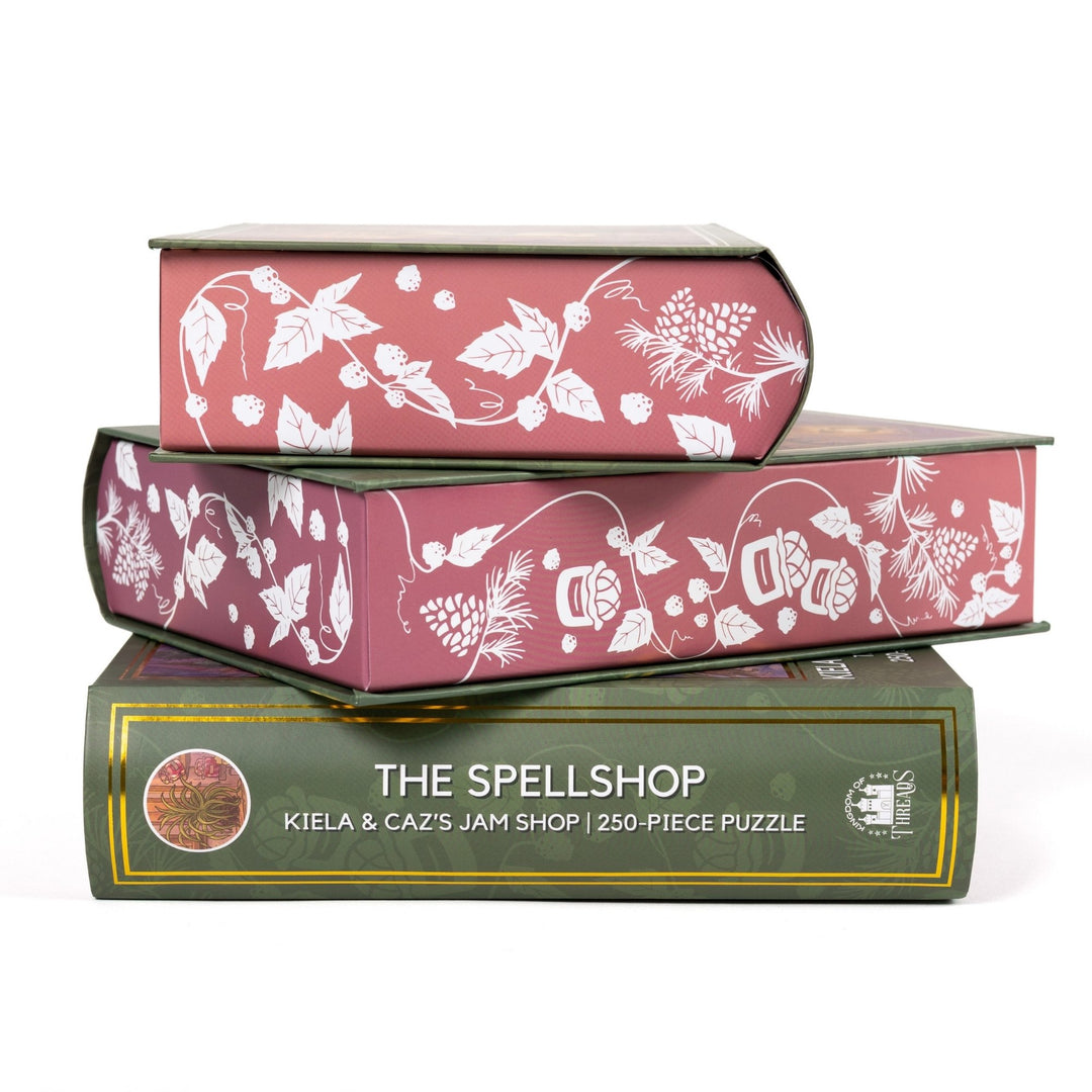 Stack of 3 puzzle boxes showing all sides. Pink edges with white raspberries and jam jars. The spine of the box reads The Spellshop Kiela and Caz’s Jam Shop 250-piece puzzle.