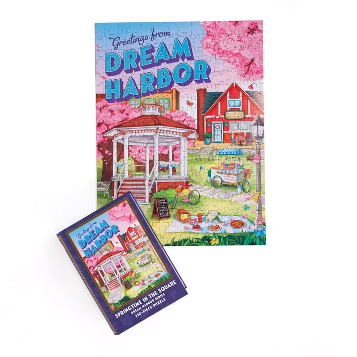 Completed puzzle of a gazebo in spring and purple, book-shaped box with matching art for Springtime in the Square Dream Harbor Series 250-piece puzzle.