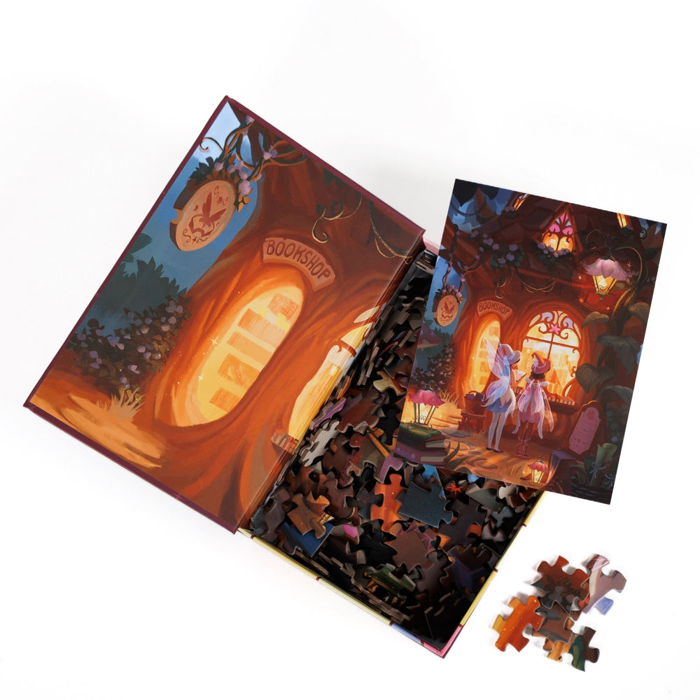 An open book-shaped box reveals puzzle pieces. Inner art on the top flap of a glowing bookstore window. An art print of two fairies looking into a woodland bookshop atop the pieces.