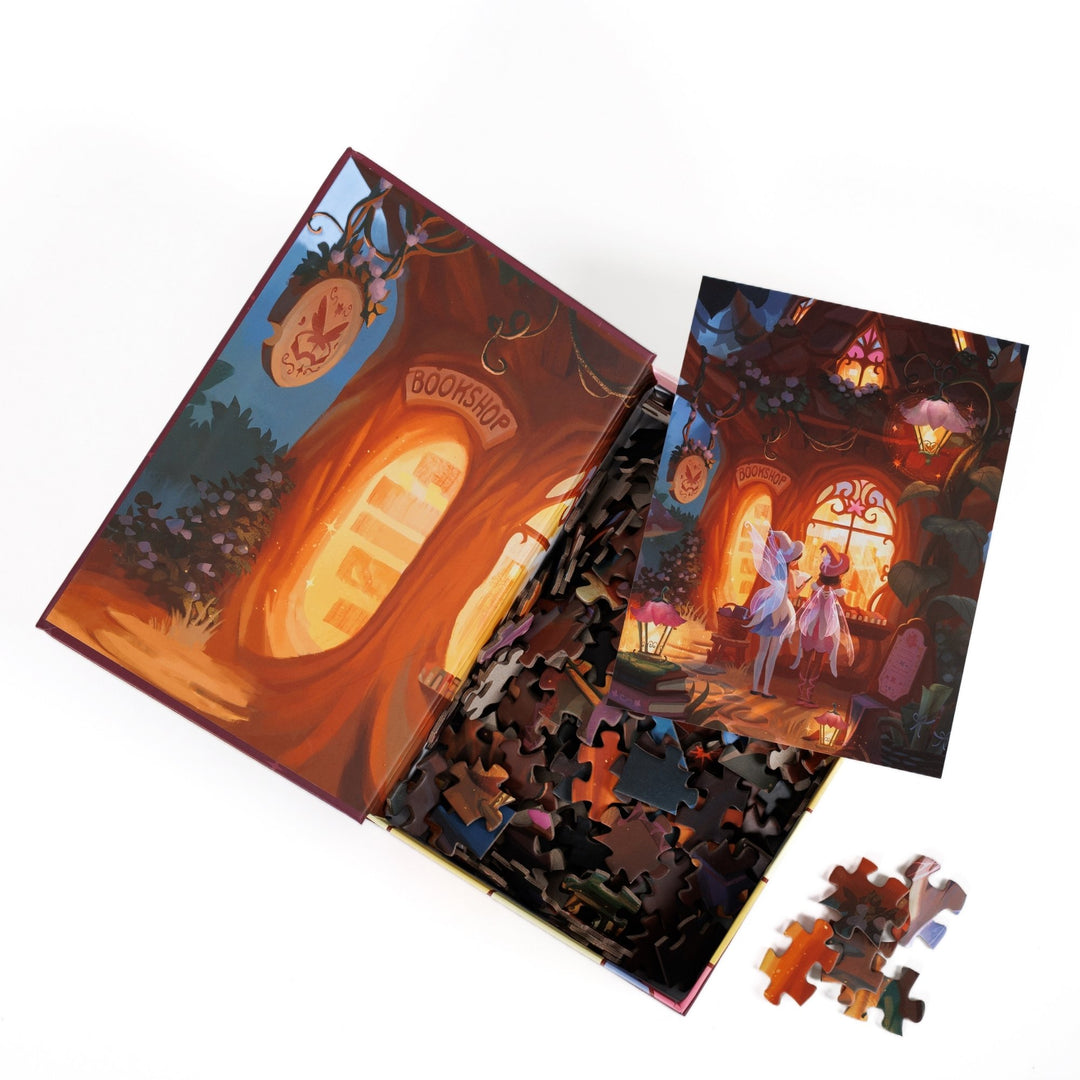 An open book-shaped box reveals puzzle pieces. Inner art on the top flap of a glowing bookstore window. An art print of two fairies looking into a woodland bookshop atop the pieces.