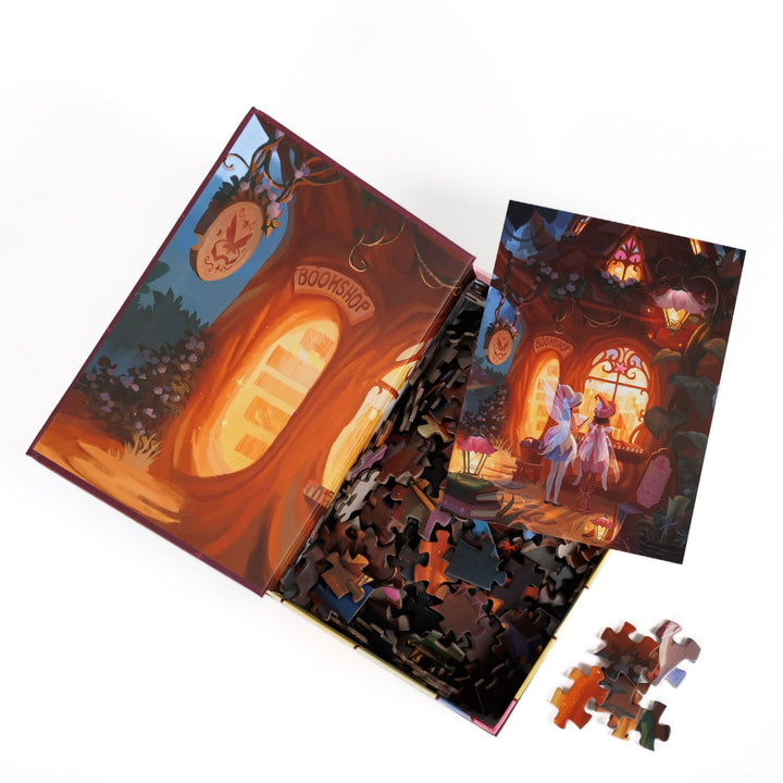 An open book-shaped box reveals puzzle pieces. Inner art on the top flap of a glowing bookstore window. An art print of two fairies looking into a woodland bookshop atop the pieces.