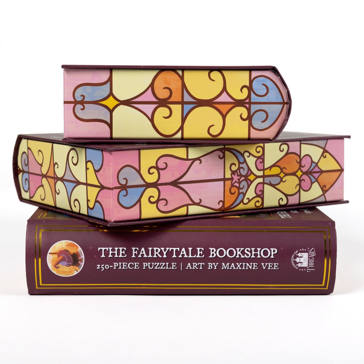 Stack of 3 puzzle boxes showing all sides. Pastel stained glass edges and the spine of the box reads ‘The Fairytale Bookshop 250-piece puzzle  Art by Maxine Vee.’