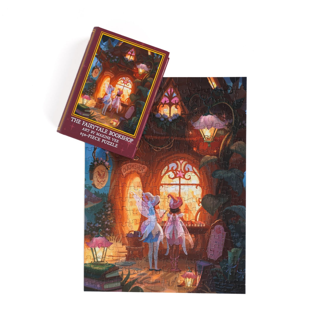 Full completed puzzle of two fairies looking into the window of a bookstore and magenta, book-shaped box with matching art for ‘The Fairytale Bookshop Art by Maxine Vee 250-piece puzzle.’