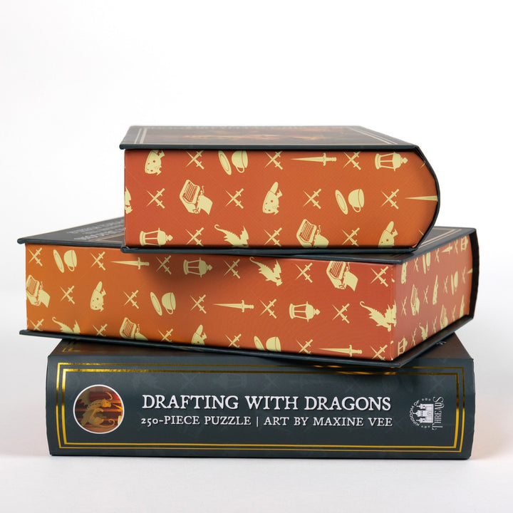 Stack of 3 puzzle boxes showing all sides. Orange edges with yellow fantasy designs. The spine of the box reads ‘Drafting with Dragons 250-piece puzzle Art by Maxine Vee.’