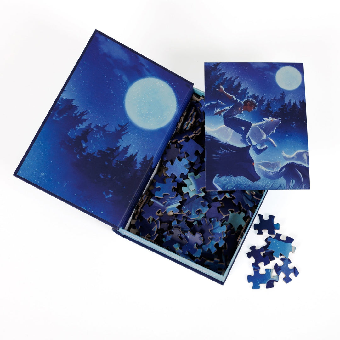 An open book-shaped box reveals puzzle pieces. Inner art on the top flap a forest and full moon. An art print of Ox running with wolves atop the pieces.