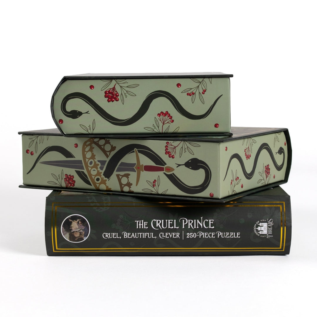 Stack of 3 puzzle boxes showing sides. Green edges with snake, sword, and crown. The spine of the box reads The Cruel Prince Cruel, Beautiful, Clever 250-piece puzzle.
