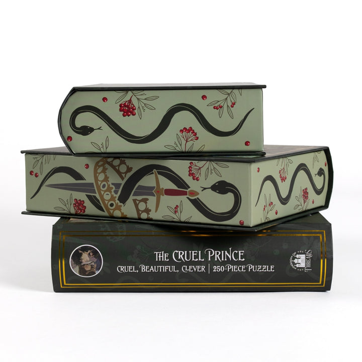 Stack of 3 puzzle boxes showing sides. Green edges with snake, sword, and crown. The spine of the box reads The Cruel Prince Cruel, Beautiful, Clever 250-piece puzzle.
