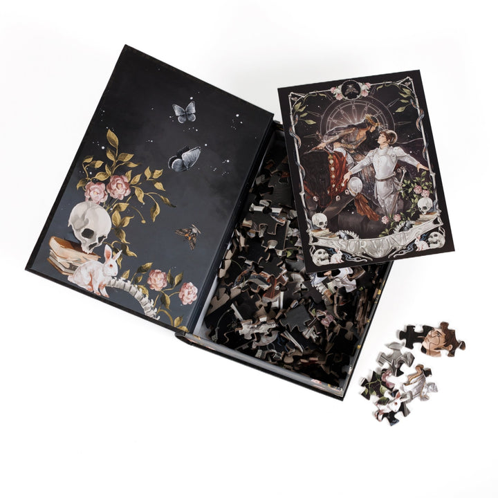 An open book-shaped box reveals puzzle pieces. Inner art on the top flap dark academia props and a skull. An art print of Alex Stern and Darlington atop the pieces.