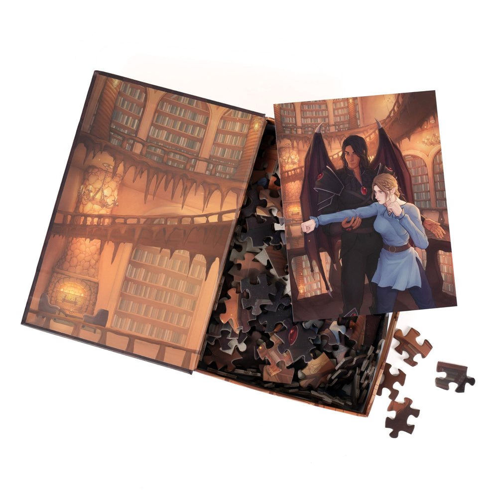 An open book-shaped box reveals puzzle pieces. Inner art on the top flap of a library. An art print of Nesta and Cassian atop the pieces.