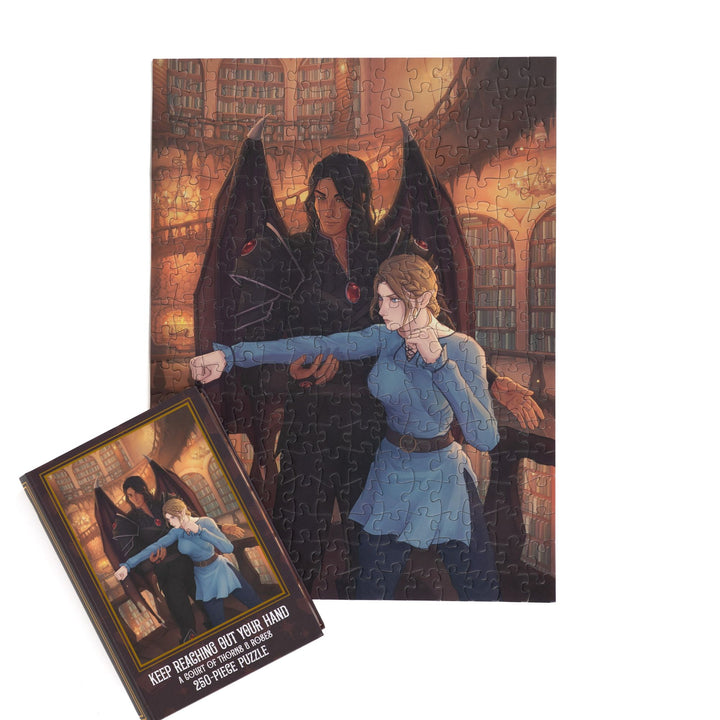 Completed puzzle of Nesta and Cassian and brown, book-shaped box with matching art for A Court of Thorns and Roses Keep Reaching Out Your Hand 250-piece puzzle.

