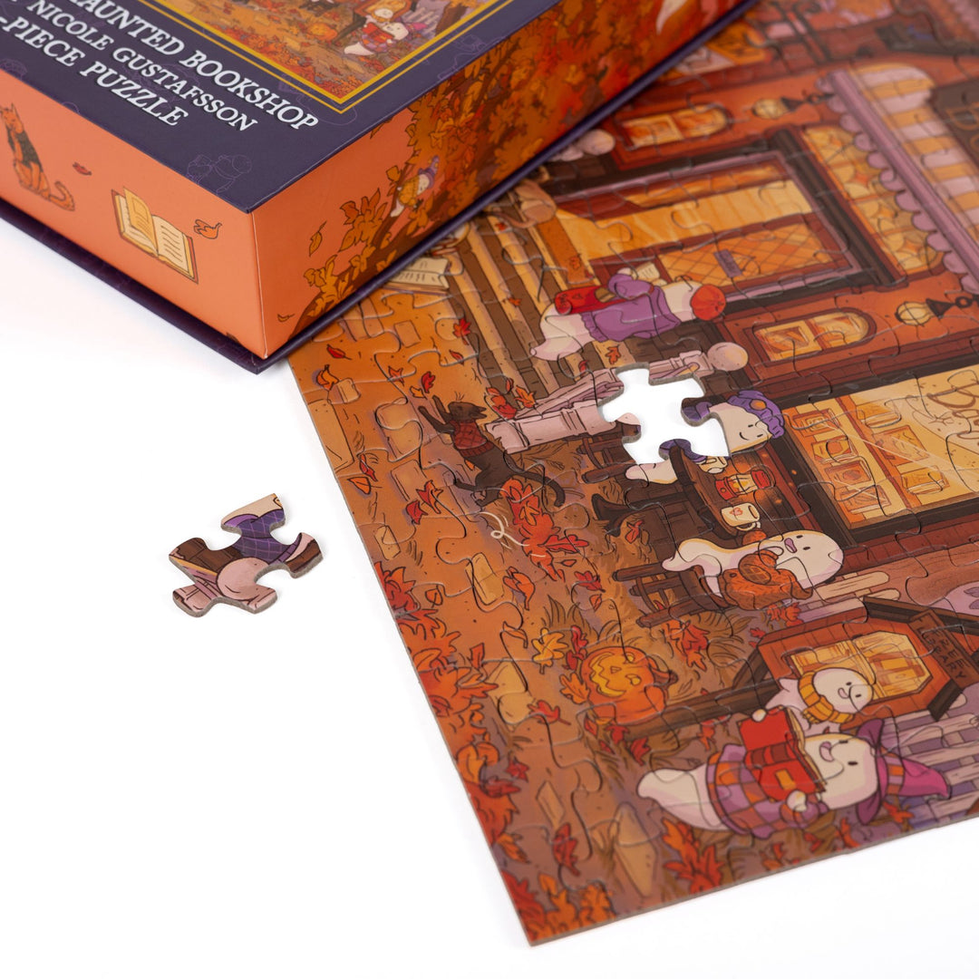 Close up of completed puzzle of cozy bookshop with cute ghosts, with one piece missing.
