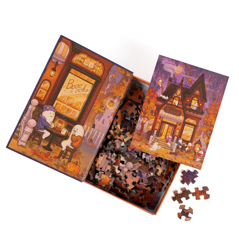 An open book-shaped box reveals puzzle pieces. Inner art on the top flap of two ghosts at a table. An art print of the haunted bookshop atop the pieces.
