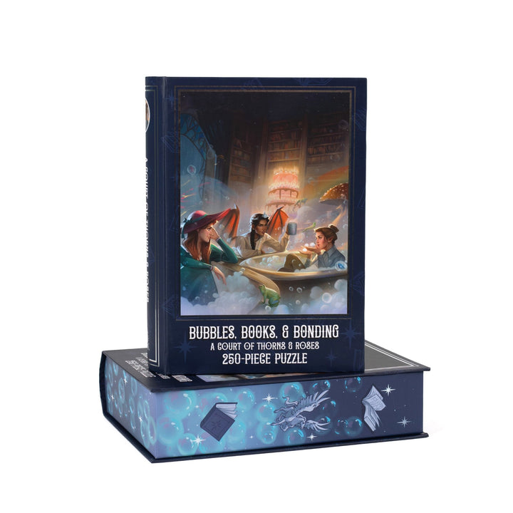 Book-shaped blue box for Bubbles, Books, and Bonding, A Court of Thorns and Roses 250-piece puzzle. Art on the front is of Nesta, Gwyn, and Emerie, each in a tub full of bubbles.