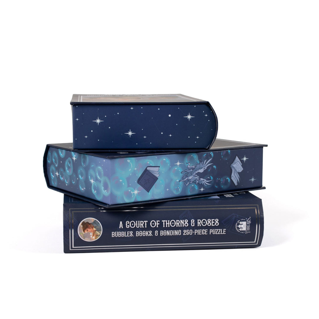 Stack of 3 puzzle boxes showing all sides. Blue edges with bubbles, books, and mini pegasus. The spine of the box reads A Court of Thorns and Roses, Bubbles, Books, and Bonding 250-piece puzzle.