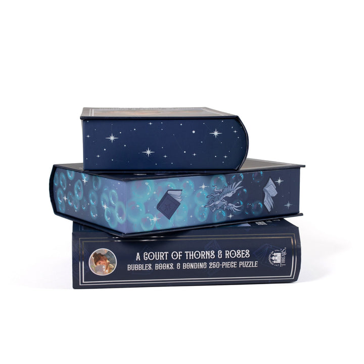 Stack of 3 puzzle boxes showing all sides. Blue edges with bubbles, books, and mini pegasus. The spine of the box reads A Court of Thorns and Roses, Bubbles, Books, and Bonding 250-piece puzzle.