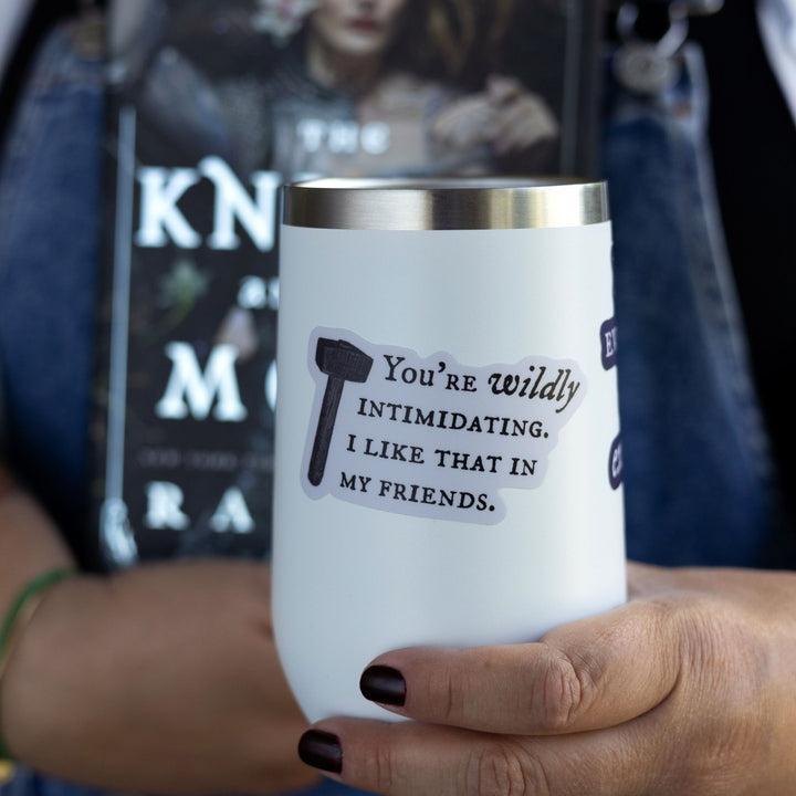 Quote sticker from Knight and the Moth ‘You’re wildly intimidating. I like that in my friends’ on a white tumbler. Light purple sticker with dark text and a hammer.