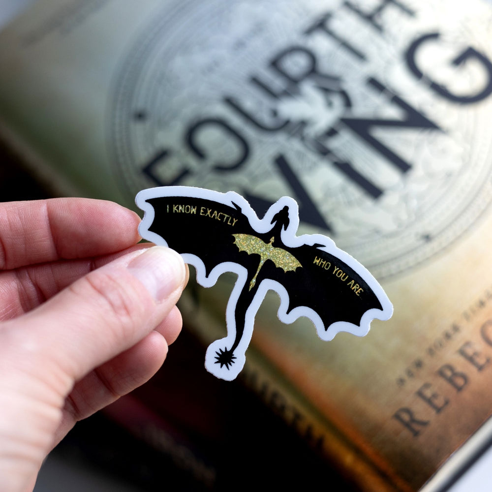 Sticker of a black dragon & holographic gold dragon in flight, held over Fourth Wing. Quote on wings: I know exactly who you are.