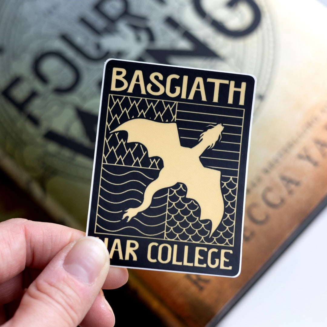  Sticker of a black & gold Basgiath emblem, featuring a gold dragon flying over the quadrant symbol, held over Fourth Wing.
