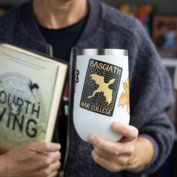 Sticker of a black & gold Basgiath emblem, featuring a gold dragon flying over the quadrant symbol, on a white tumbler.

