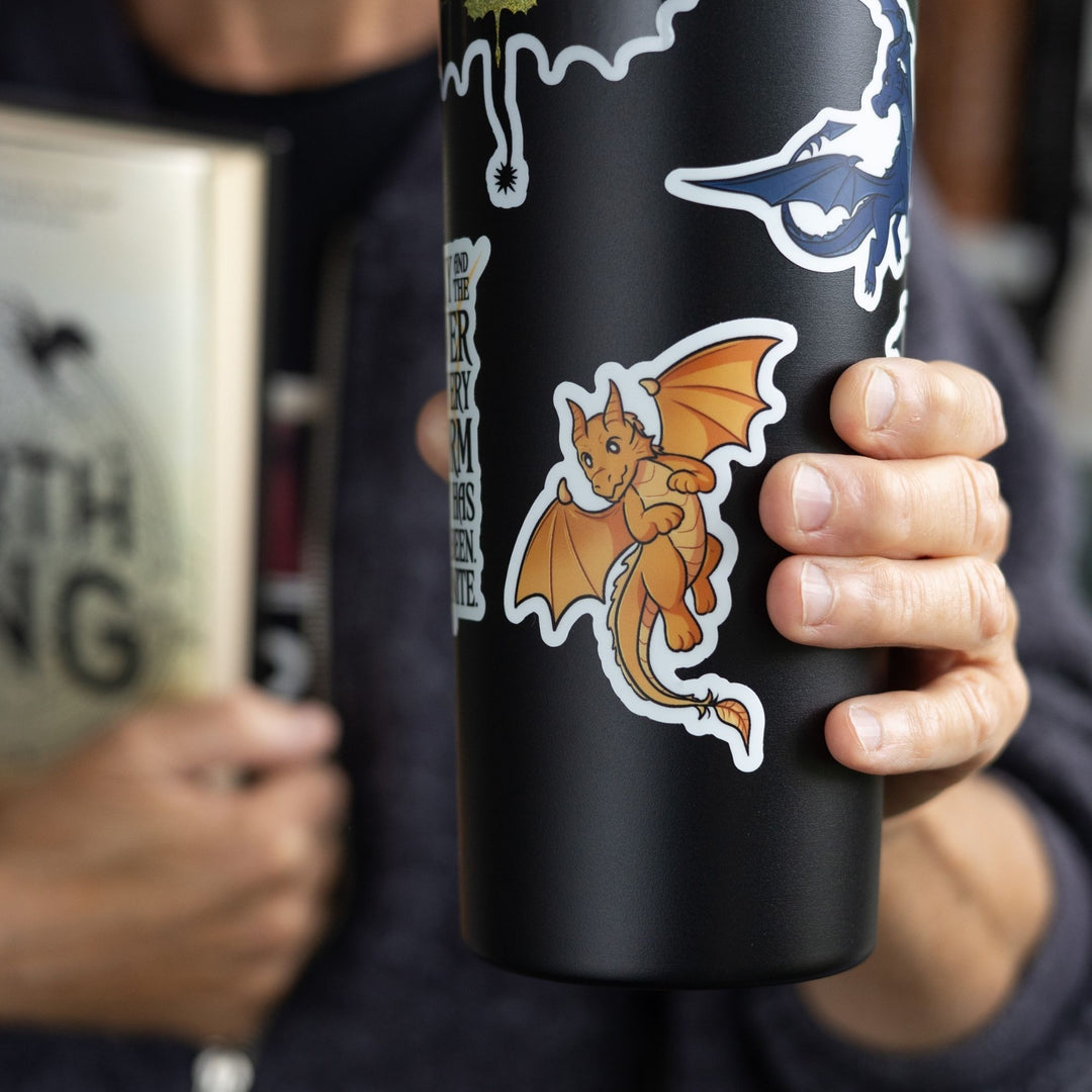 Sticker  of Andarna, a gold baby dragon, as a vinyl sticker. Sticker is on a black tumbler
