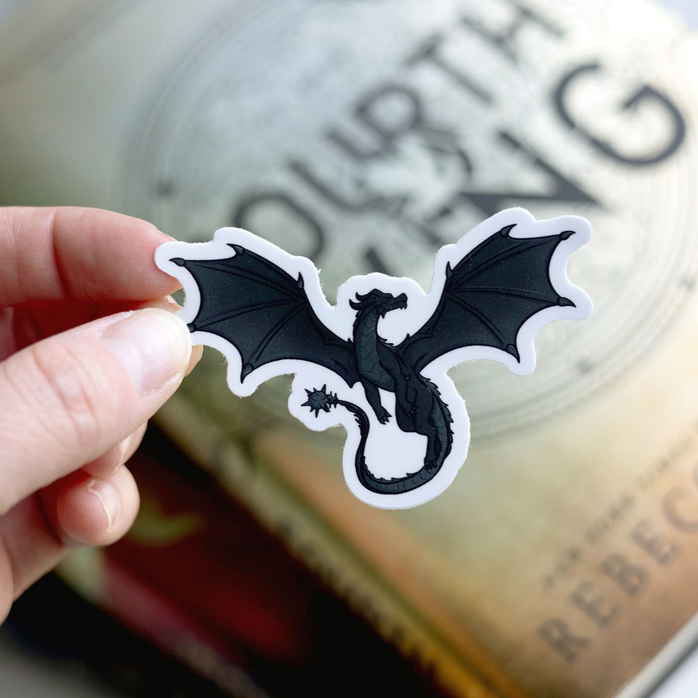 Sticker of Tairn, a magnificent black dragon, as a vinyl sticker. Sticker is held over Fourth Wing by Rebecca Yarros.