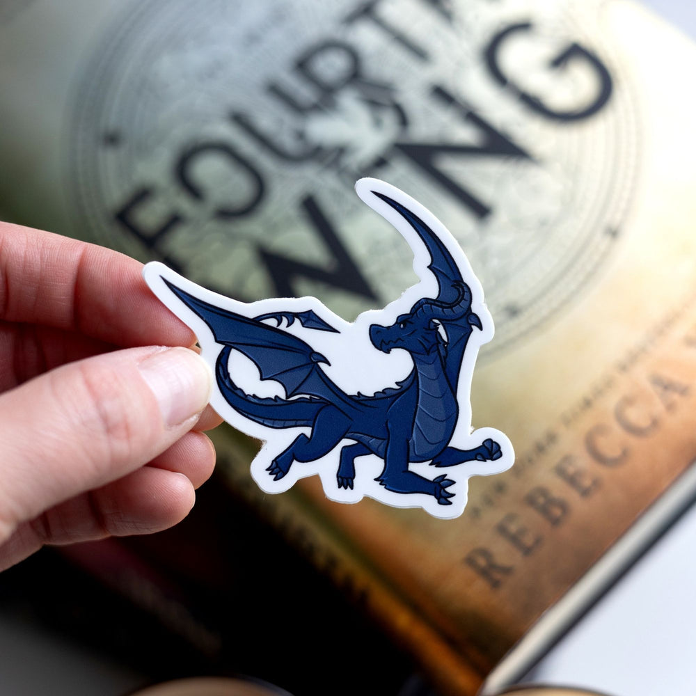 Sticker of Sgaeyl, a navy blue dragon, in flight as a vinyl sticker. Sticker is held over Fourth Wing by Rebecca Yarros.