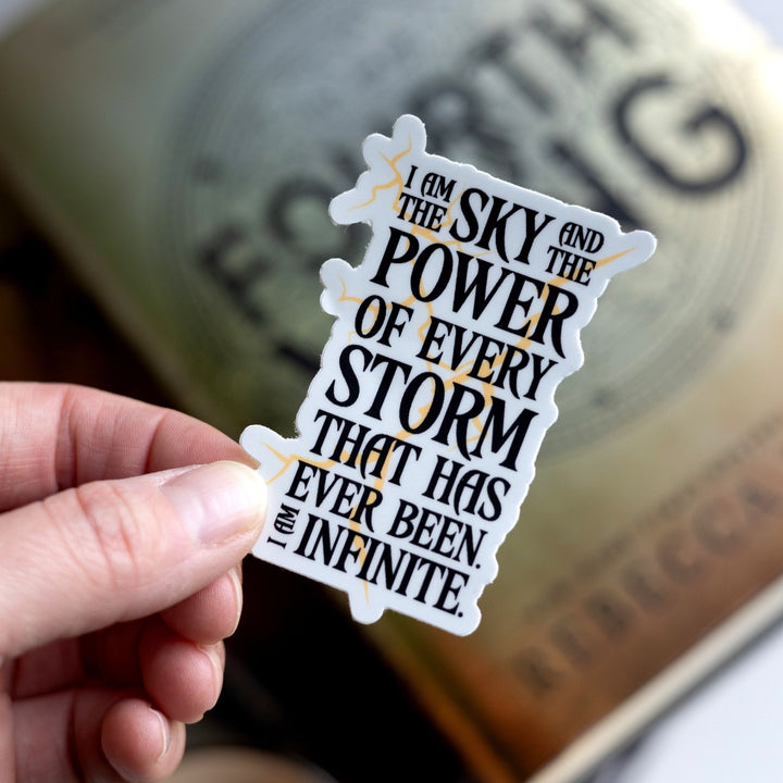  Quote sticker: ‘I am the sky and the power of every storm that has ever been. I am infinite.’ Black text over lightning strikes, held over Fourth Wing.
