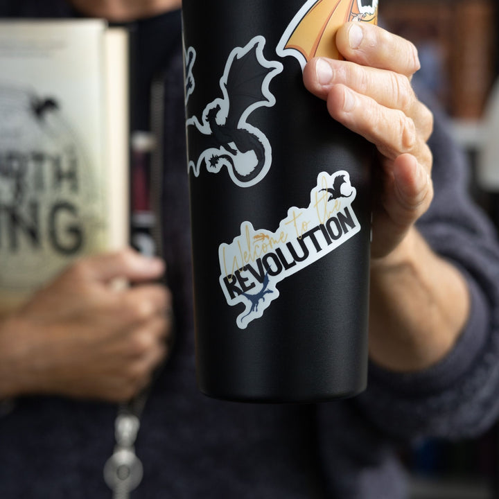 Quote sticker: Welcome to the revolution. Text flanked by a black, blue, and gold dragon. On a black tumbler